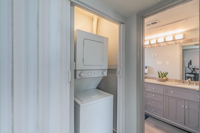 clothes washing area featuring stacked washing maching and dryer, sink, and light hardwood / wood-style floors