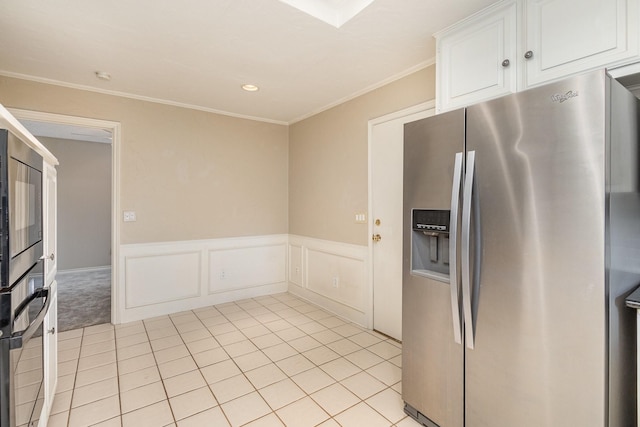 kitchen with light tile patterned floors, appliances with stainless steel finishes, ornamental molding, wainscoting, and white cabinetry