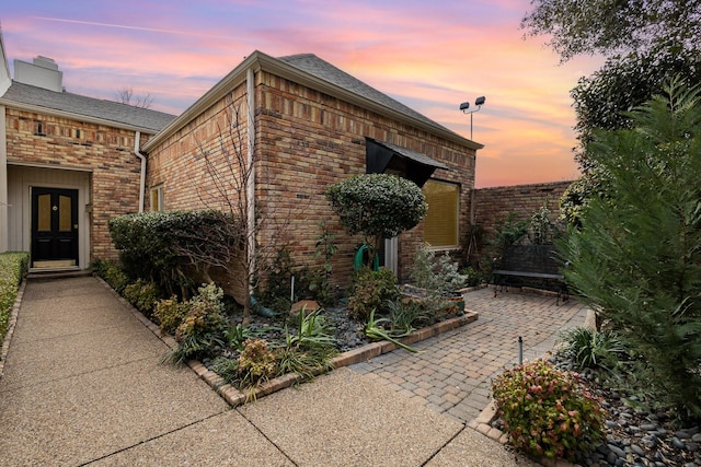 property exterior at dusk featuring brick siding and a patio