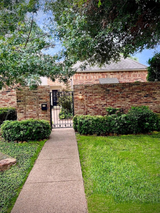 exterior space with a gate, brick siding, and a front lawn