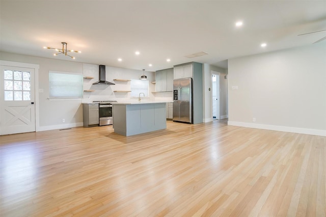 kitchen with wall chimney range hood, appliances with stainless steel finishes, gray cabinets, and a kitchen island