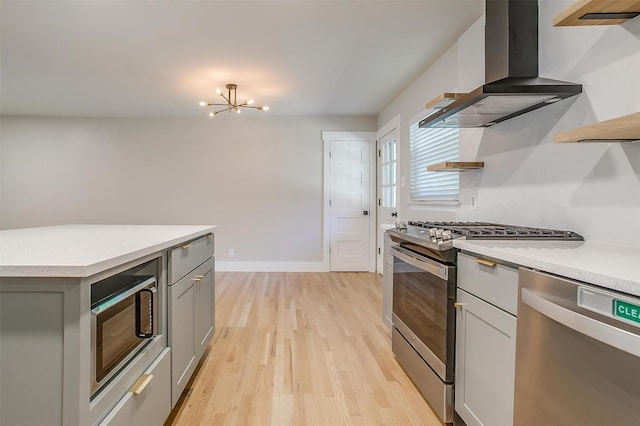 kitchen featuring an inviting chandelier, light hardwood / wood-style floors, stainless steel appliances, gray cabinetry, and wall chimney range hood