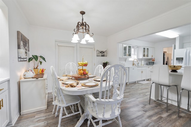 dining room with sink, crown molding, wood-type flooring, and a chandelier