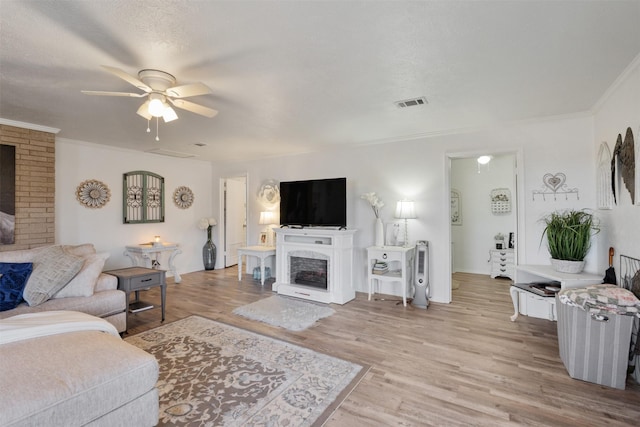 living room featuring ceiling fan, ornamental molding, a fireplace, and light hardwood / wood-style flooring