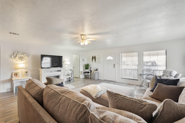 living room with ceiling fan, light hardwood / wood-style floors, and a textured ceiling