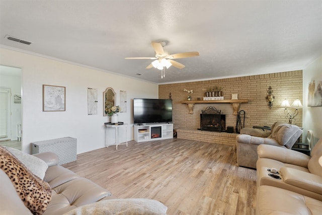 living room with crown molding, a fireplace, ceiling fan, and light wood-type flooring