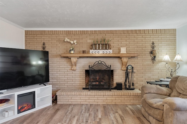 living room featuring wood-type flooring, ornamental molding, a large fireplace, and a textured ceiling