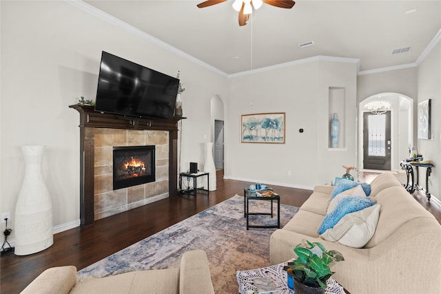 living room with ceiling fan, dark hardwood / wood-style floors, crown molding, and a tiled fireplace