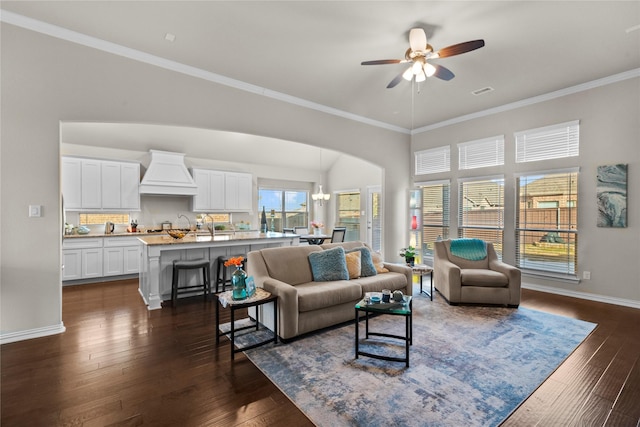 living room with ceiling fan with notable chandelier, dark wood-type flooring, and crown molding