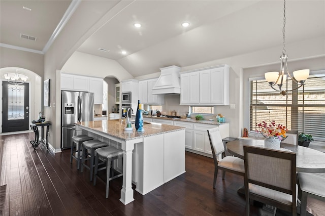 kitchen featuring custom exhaust hood, an inviting chandelier, a kitchen island with sink, stainless steel appliances, and white cabinets