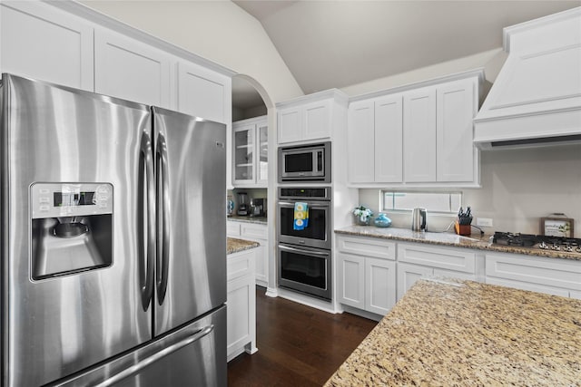 kitchen with vaulted ceiling, white cabinetry, stainless steel appliances, custom range hood, and light stone counters