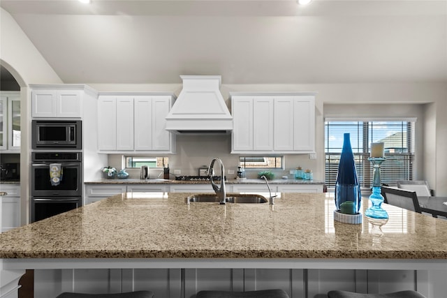 kitchen with premium range hood, a kitchen bar, stainless steel microwave, white cabinets, and sink