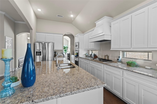 kitchen with white cabinets, appliances with stainless steel finishes, custom exhaust hood, sink, and light stone counters