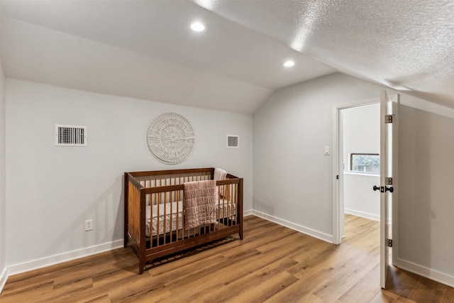 bedroom featuring vaulted ceiling, a textured ceiling, hardwood / wood-style flooring, and a crib