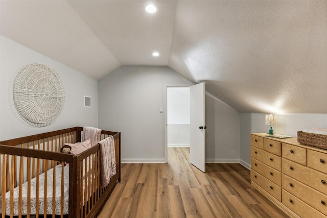 bedroom featuring vaulted ceiling, a crib, a textured ceiling, and hardwood / wood-style flooring