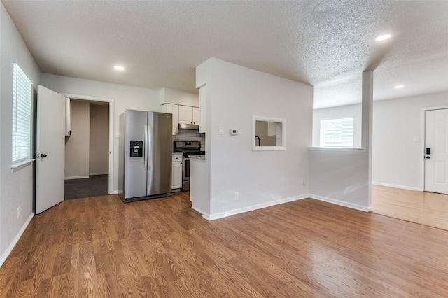 kitchen with white cabinetry, hardwood / wood-style flooring, appliances with stainless steel finishes, decorative backsplash, and a textured ceiling