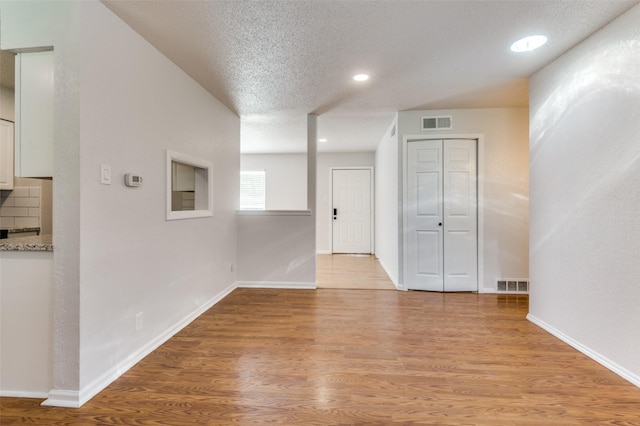 empty room with a textured ceiling and light hardwood / wood-style flooring