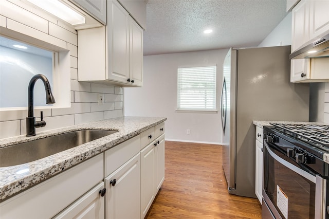 kitchen with light hardwood / wood-style floors, gas range, a textured ceiling, white cabinets, and sink