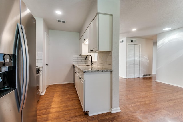 kitchen with stainless steel fridge, tasteful backsplash, light stone countertops, white cabinets, and sink