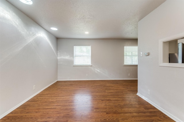 spare room featuring dark wood-type flooring, a wealth of natural light, and a textured ceiling