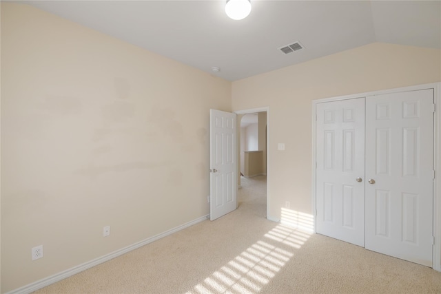 unfurnished bedroom with light colored carpet, a closet, and vaulted ceiling