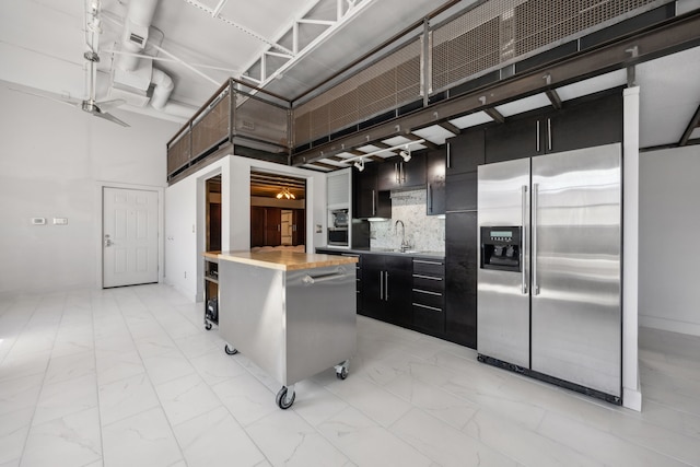 kitchen featuring a center island, decorative backsplash, a towering ceiling, sink, and stainless steel fridge