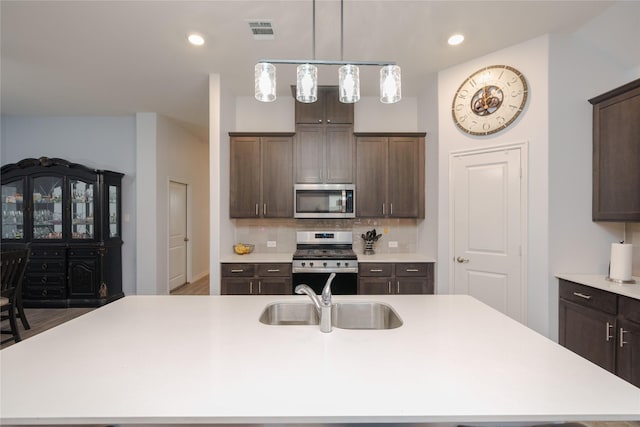 kitchen with dark brown cabinetry, stainless steel appliances, sink, backsplash, and a center island with sink