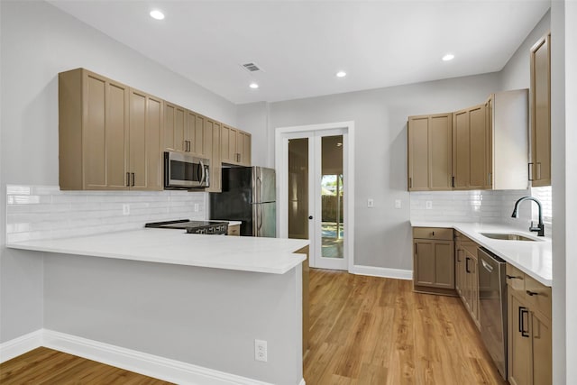 kitchen featuring stainless steel appliances, light hardwood / wood-style floors, sink, decorative backsplash, and kitchen peninsula