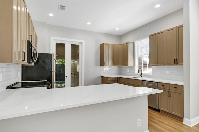 kitchen with light stone countertops, appliances with stainless steel finishes, sink, kitchen peninsula, and light wood-type flooring