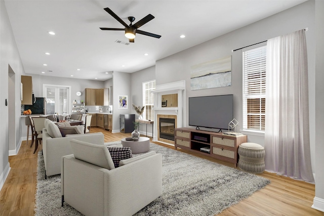 living room with ceiling fan, sink, a tile fireplace, and light wood-type flooring