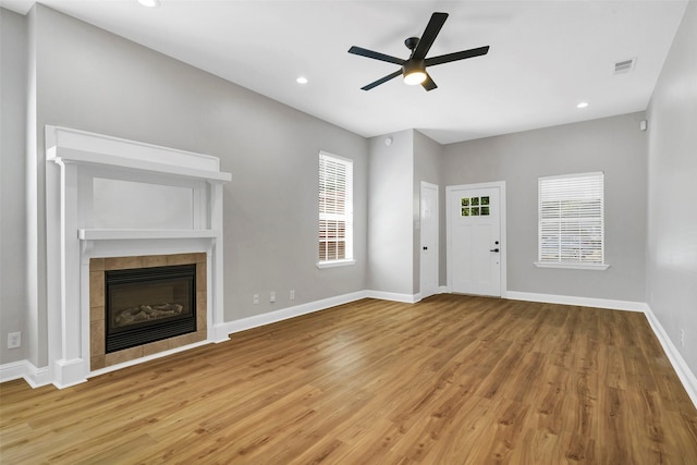 unfurnished living room featuring ceiling fan, a tiled fireplace, and hardwood / wood-style floors