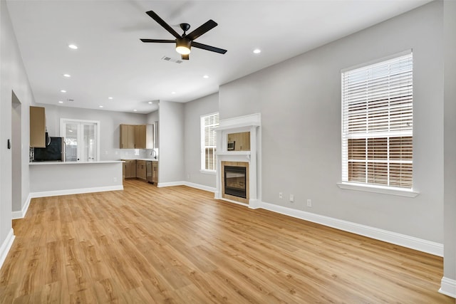 unfurnished living room with light wood-type flooring, ceiling fan, a tile fireplace, and sink