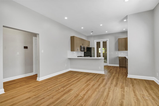 kitchen with light wood-type flooring, kitchen peninsula, tasteful backsplash, and stainless steel appliances