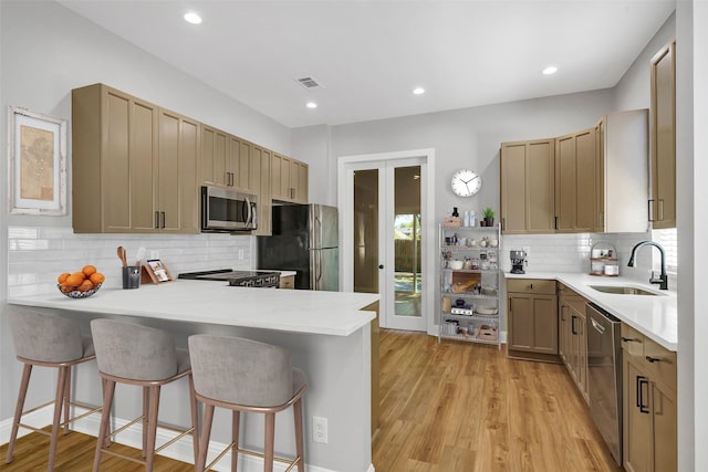 kitchen featuring light hardwood / wood-style floors, kitchen peninsula, a kitchen bar, sink, and appliances with stainless steel finishes