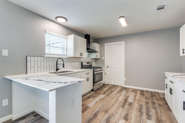 kitchen with kitchen peninsula, sink, stainless steel range with gas stovetop, white cabinets, and wall chimney exhaust hood