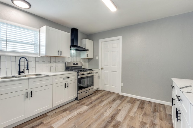 kitchen featuring wall chimney range hood, white cabinetry, decorative backsplash, sink, and stainless steel range with gas stovetop