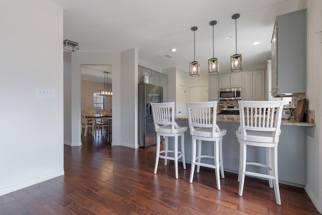 kitchen with a kitchen bar, appliances with stainless steel finishes, decorative backsplash, gray cabinetry, and dark hardwood / wood-style floors