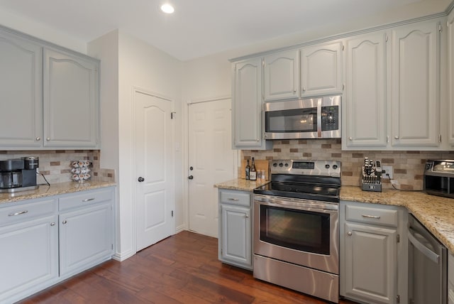 kitchen featuring dark wood-type flooring, stainless steel appliances, decorative backsplash, and light stone counters