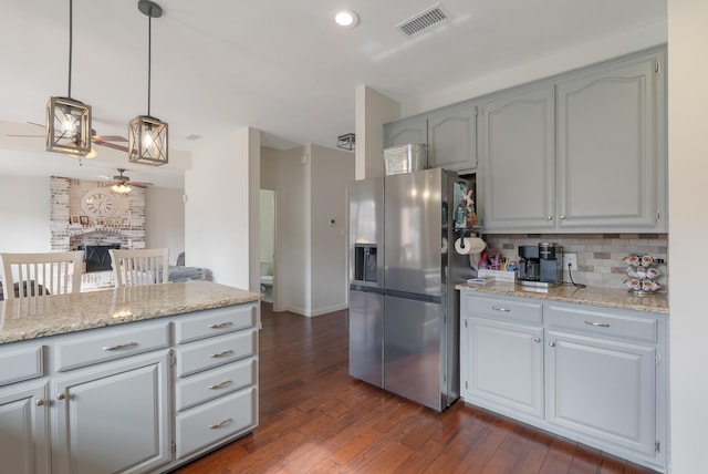 kitchen featuring stainless steel refrigerator with ice dispenser, backsplash, dark hardwood / wood-style flooring, a fireplace, and pendant lighting