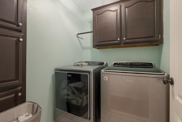 clothes washing area featuring tile patterned flooring, washer and dryer, and cabinets