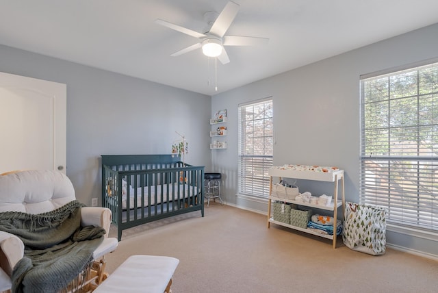 carpeted bedroom with ceiling fan and a crib