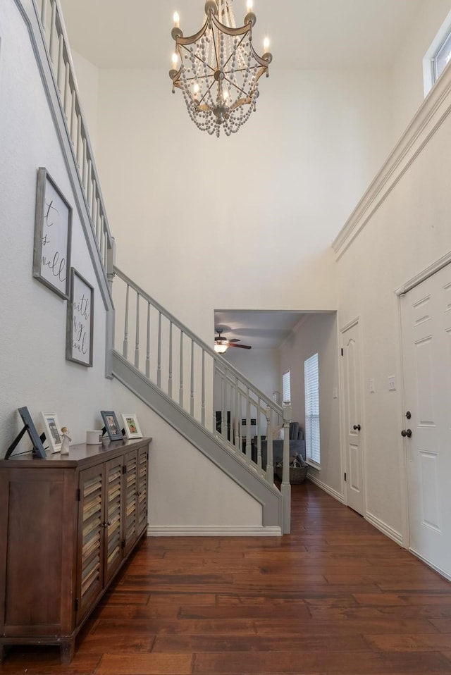 entryway with dark hardwood / wood-style floors, ceiling fan with notable chandelier, and a high ceiling