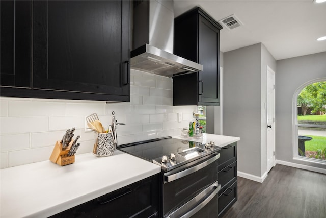 kitchen with decorative backsplash, dark hardwood / wood-style floors, wall chimney range hood, and range with two ovens