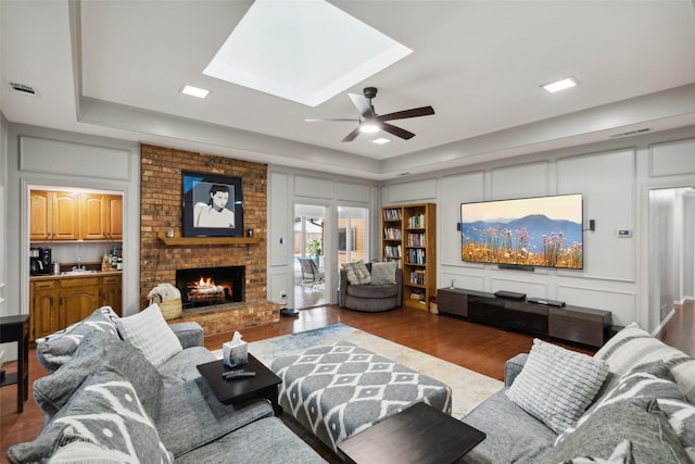 living room featuring wood-type flooring, a skylight, sink, a raised ceiling, and a brick fireplace