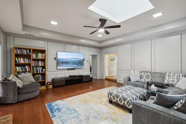 living room with a raised ceiling, ceiling fan, and dark hardwood / wood-style flooring