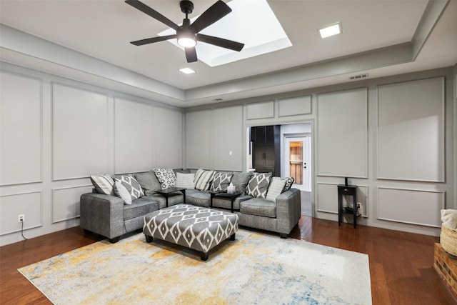 living room with a skylight, dark hardwood / wood-style flooring, a raised ceiling, and ceiling fan