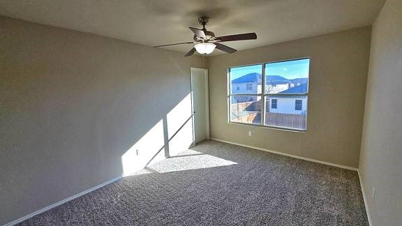 empty room featuring ceiling fan and dark carpet