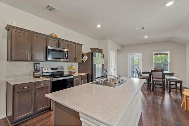 kitchen with dark brown cabinetry, stainless steel appliances, an island with sink, sink, and light stone counters