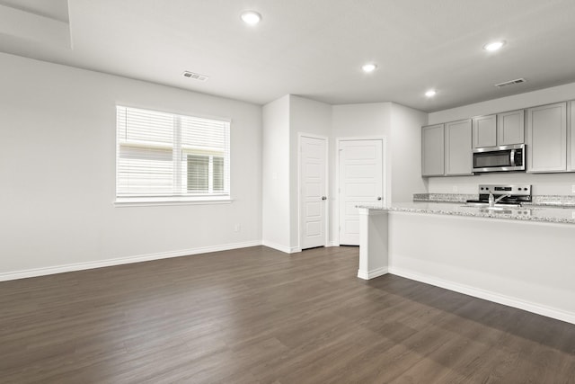 kitchen featuring gray cabinetry, appliances with stainless steel finishes, light stone counters, and dark hardwood / wood-style floors