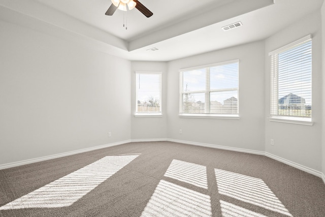 unfurnished room featuring ceiling fan, dark carpet, and a tray ceiling